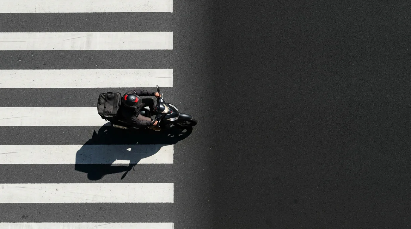 Vu du ciel, un coursier à moto franchit un passage piéton sur l’asphalte.