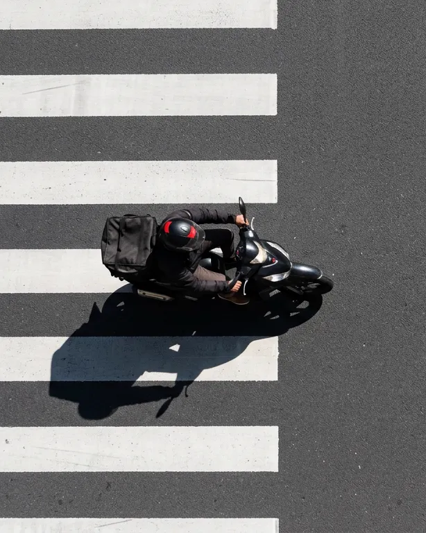 Un coursier à moto traverse un passage piéton, vu du ciel.
